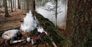 Man lighting a fire after preparing emergency shelter for the night