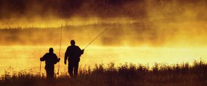 Silhouetted fly fishermen walking on bank of Madison River in Yellowstone National Park